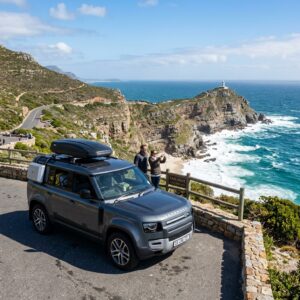 Land Rover Defender parked at Cape Point overlook with ocean cliffs and lighthouse